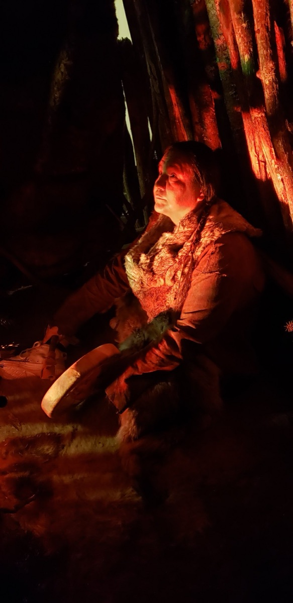 Walter seated by firelight with a hand drum