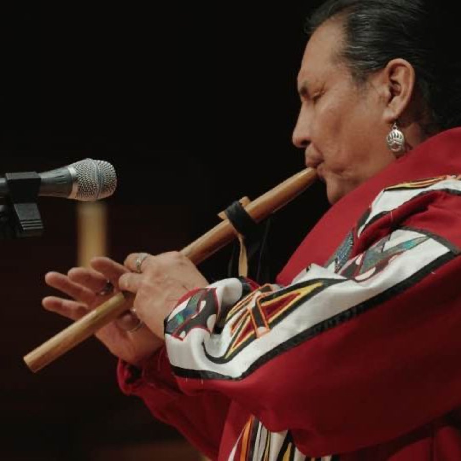 Walter playing a traditional wooden flute at a microphone