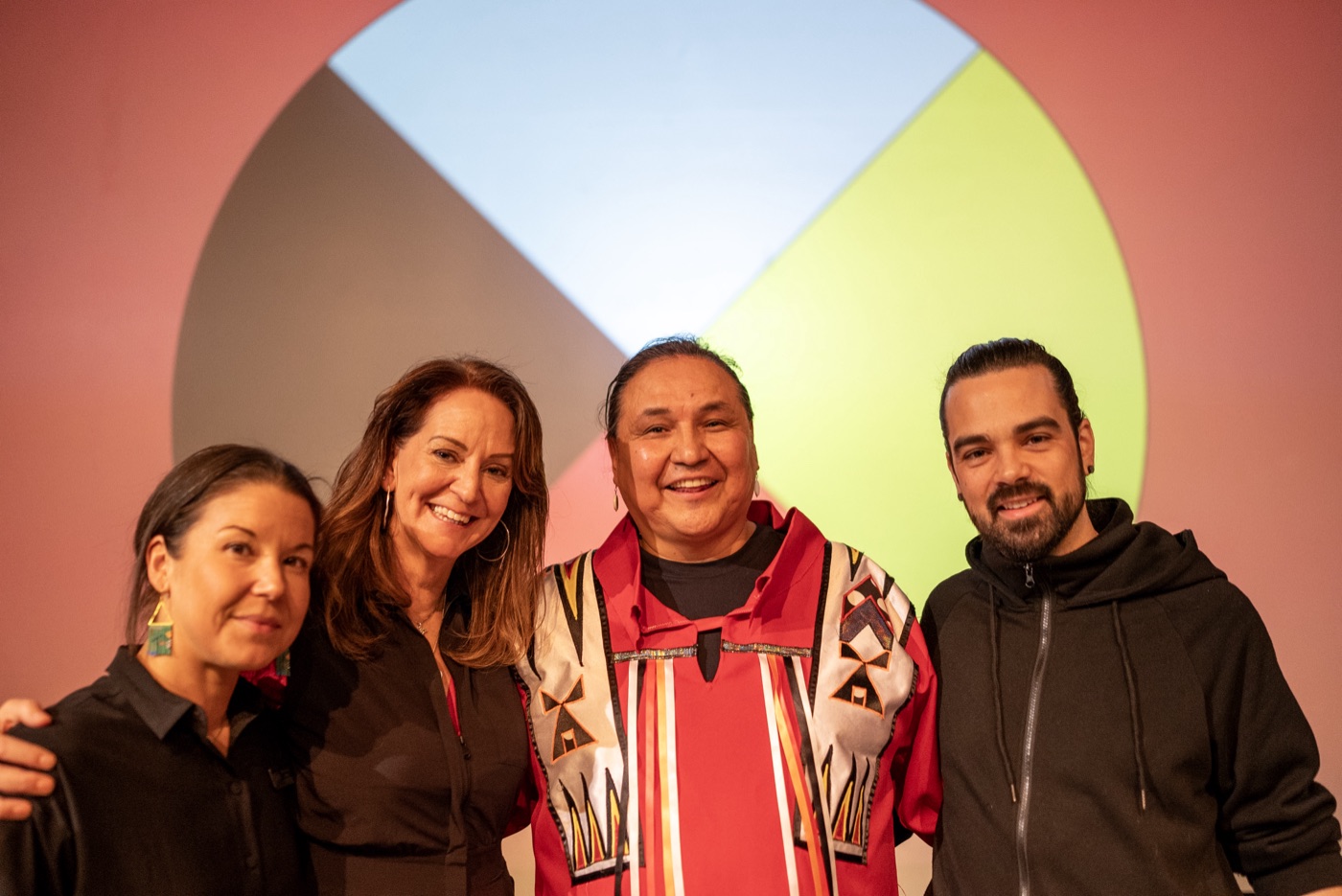 Walter smiling with friends in front of a medicine wheel backdrop