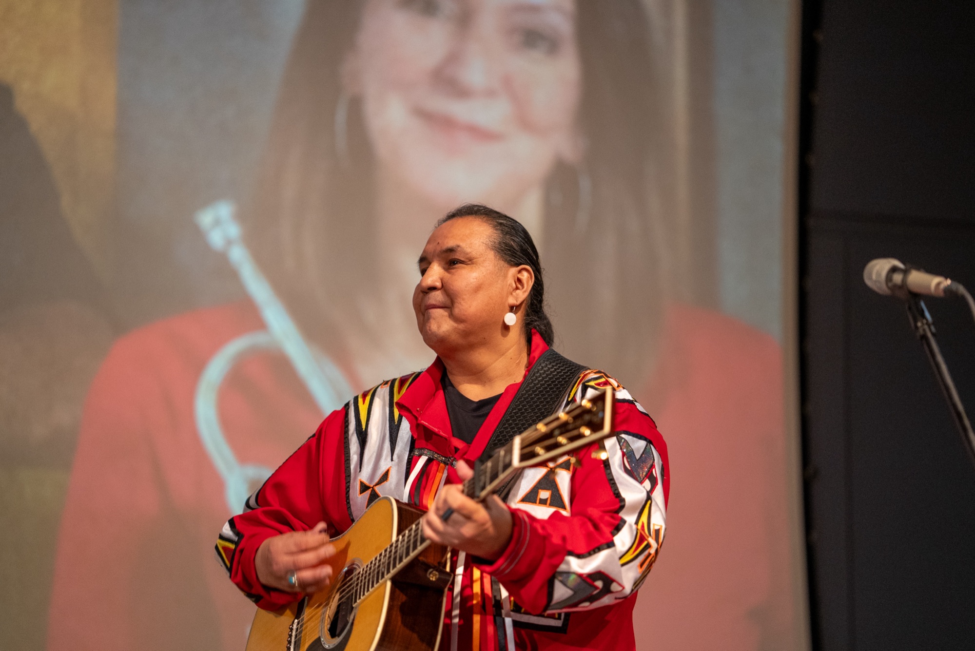 Walter performing with acoustic guitar in embroidered red regalia