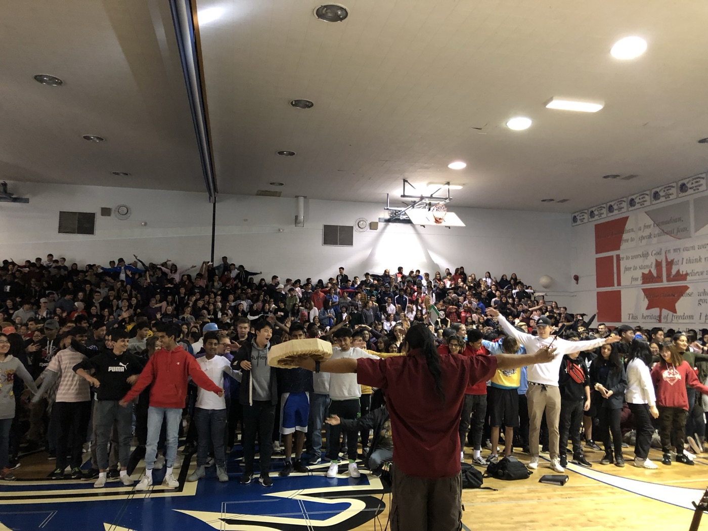 A packed school gymnasium standing arm in arm during Walter's assembly
